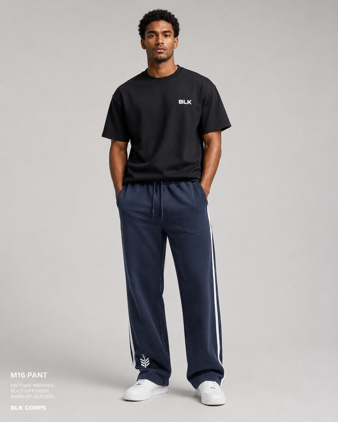 Man wearing a black t-shirt and navy tracksuit with white stripes on a gray background