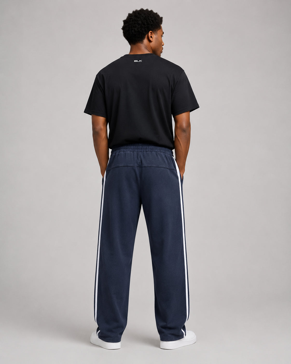 Person wearing a black t-shirt and navy tracksuit with white stripes on a gray background