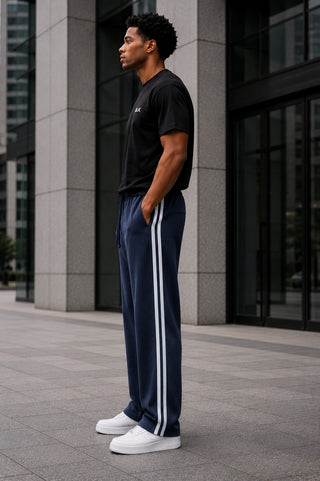 Man wearing a black t-shirt and navy tracksuit with white stripes standing in an urban setting.