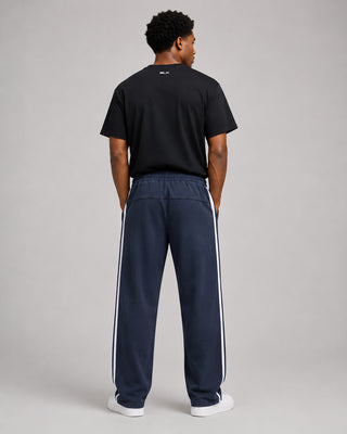 Person wearing a black t-shirt and navy tracksuit with white stripes on a gray background
