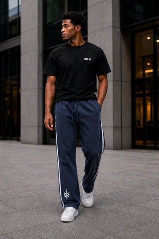 Man wearing a black t-shirt and navy tracksuit with white stripes in an urban setting